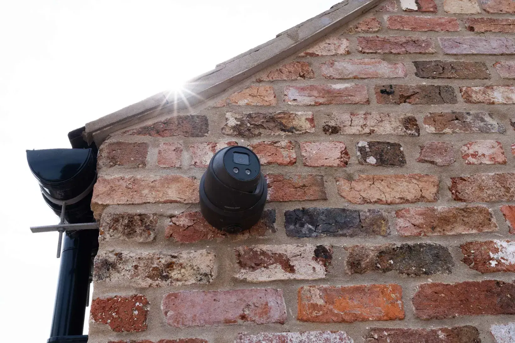 A dome camera fitted to a weathered brick gable, below the sloping verge coping